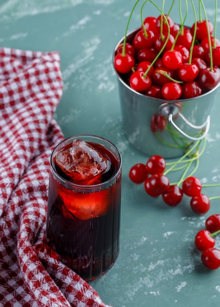 Juice in a jug with cherries high angle view on plaster and kitchen towel