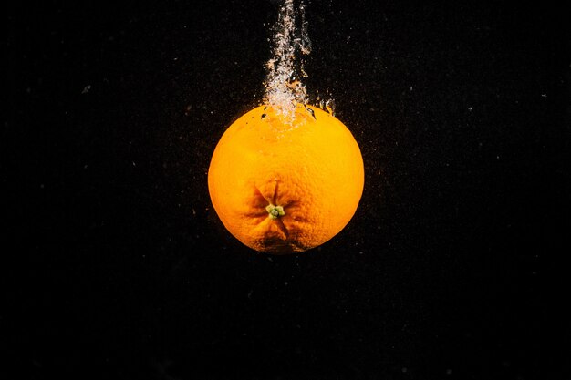 Juicy orange falls in water on black background