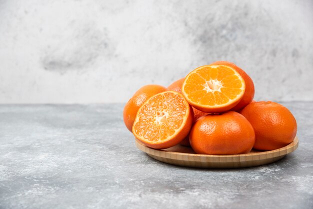 Juicy orange fruits with slices in a wooden plate on stone table .