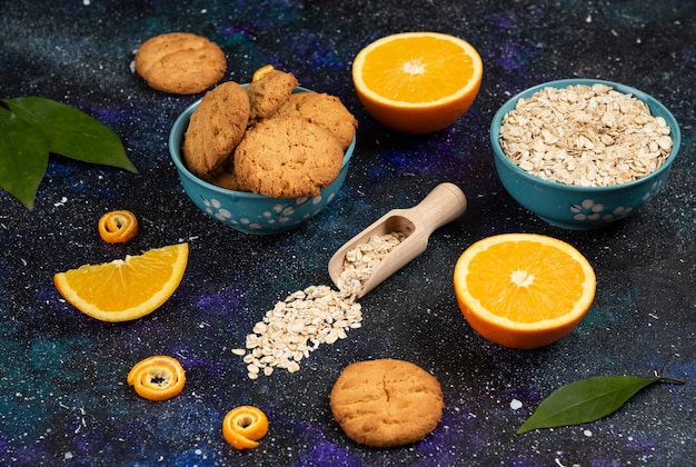 Juicy oranges with cookie and oatmeal over dark table.