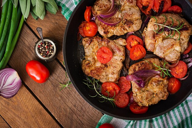 Juicy pork steak with rosemary and tomatoes on pan.