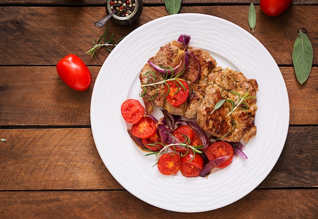 Free Photo juicy pork steak with rosemary and tomatoes on a white plate.