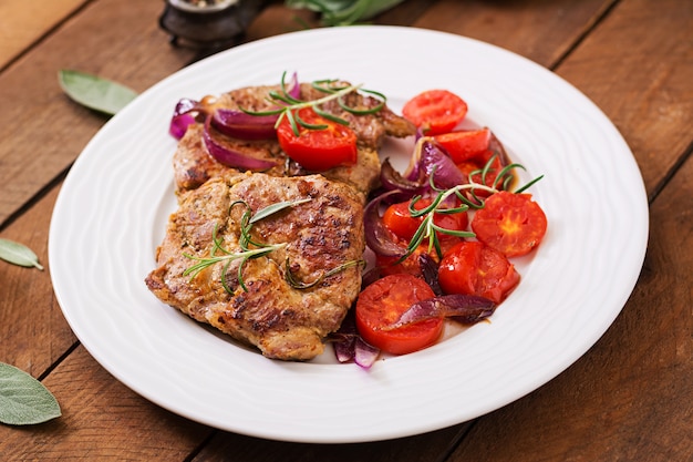 Juicy pork steak with rosemary and tomatoes on a white plate