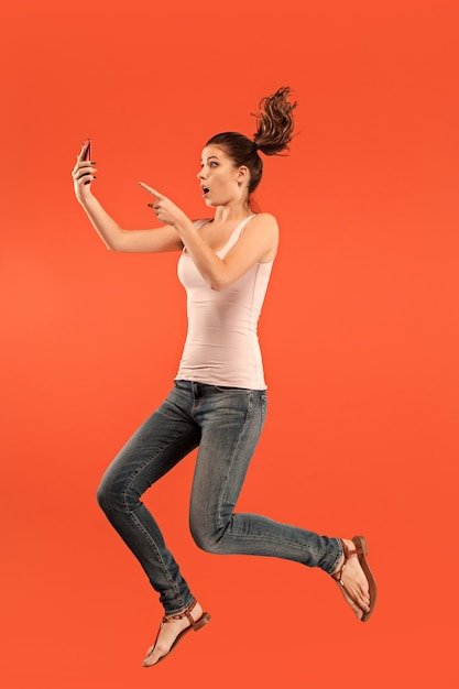 Free Photo jump of young woman over blue studio background using laptop or tablet gadget while jumping. running girl in motion or movement. human emotions and facial expressions concept.