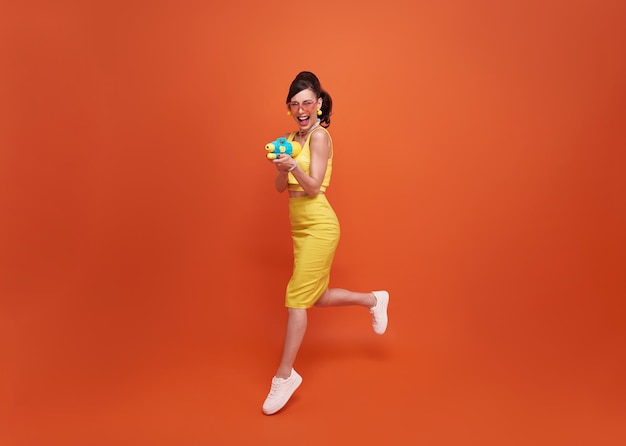 Jumping tourist woman traveling with water gun during Songkran festival studio background