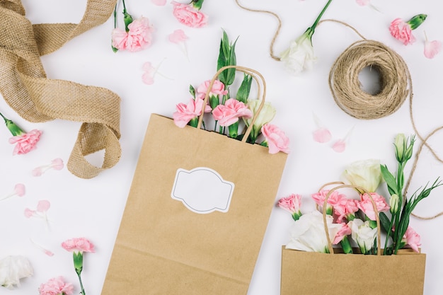 Free Photo jute ribbon; spool of thread and paper shopping bags with eustoma and carnations flowers on white background