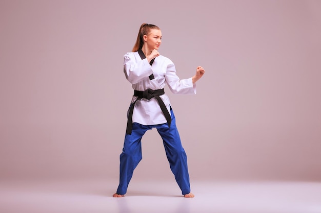 Free photo the karate girl in white kimono and black belt training karate over gray background.