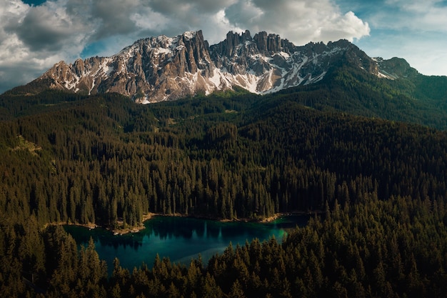 Karersee surrounded by forests and Dolomites under a cloudy sky in Italy