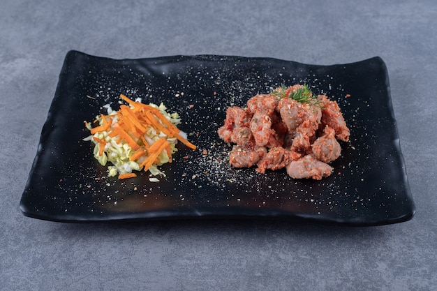 Kebab pieces and salad on black plate.