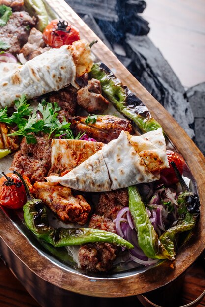 Kebab varieties with vegetables inside wooden platter.