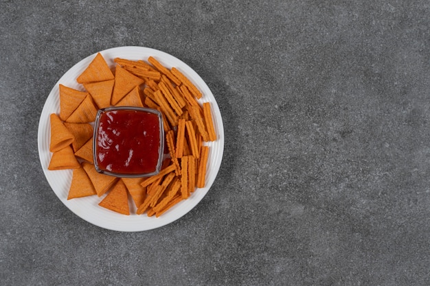 Ketchup, corn chips and dried bread on plate  on the marble surface