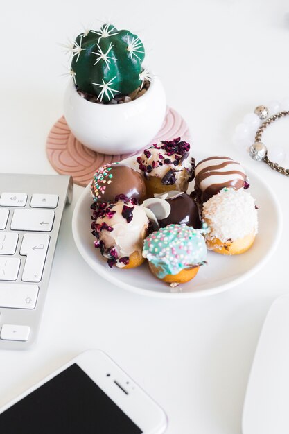 Keyboard near smartphone, armlets, houseplant and biscuits on plate