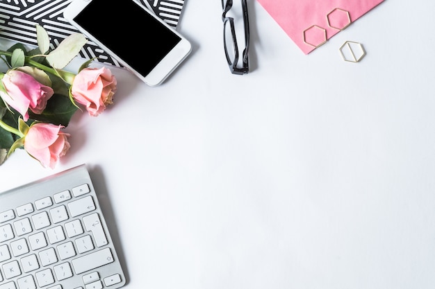 Keyboard, a smartphone, glasses and pink roses on a white surface