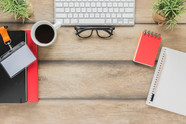 Free photo keyboard with glasses near stationary and coffee cup on table