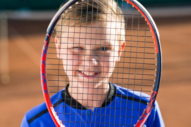 Kid covering his face with a tennis racket