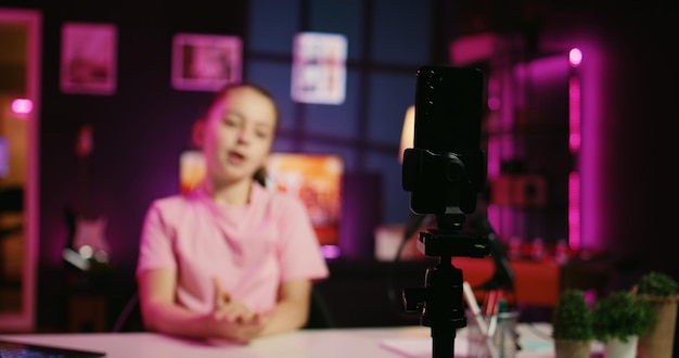 Kid entertaining followers doing content creation in pink neon lit apartment using phone on tripod