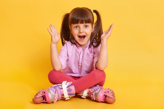 Kid girl in roller skates sits on the floor at free text