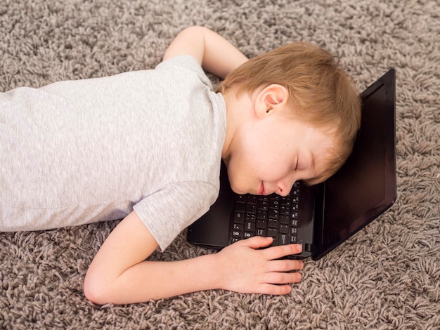 Free photo kid laying with his head on a laptop