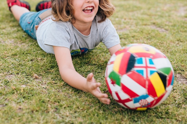 Free photo kid lying in grass and playing with ball