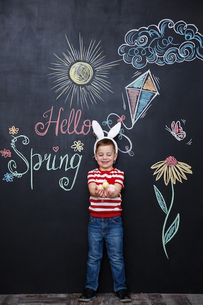 Free photo kid wearing bunny ears and holding heap of easter eggs