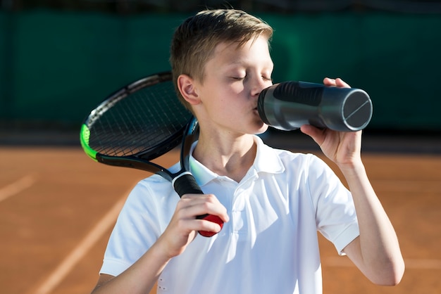 Free photo kid with racket on the shoulder and drinking water