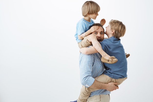 Kids fooling around with cool dad. Portrait of playful happy sons hanging on father body, having fun and playing together