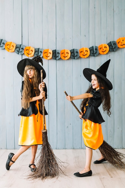 Kids in witch costumes holding broomsticks 