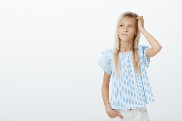 Kind adorable girl making idea how to cheer up mom. Confused concerned little child with fair hair, scratching head and looking up while thinking or planning next step, clueless and unaware