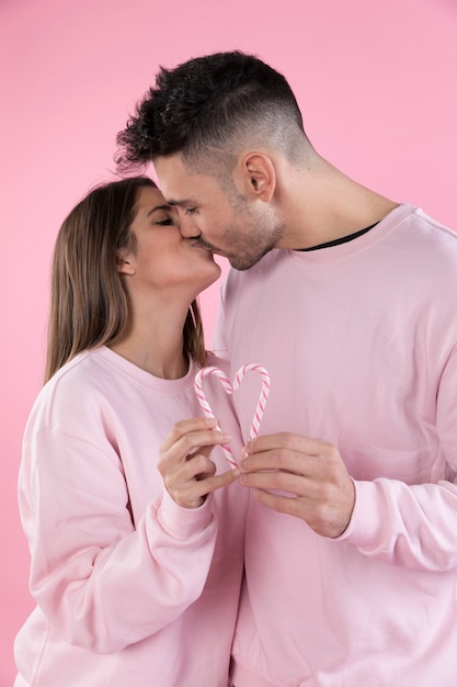 Kiss of man and woman holding candy canes in form of heart