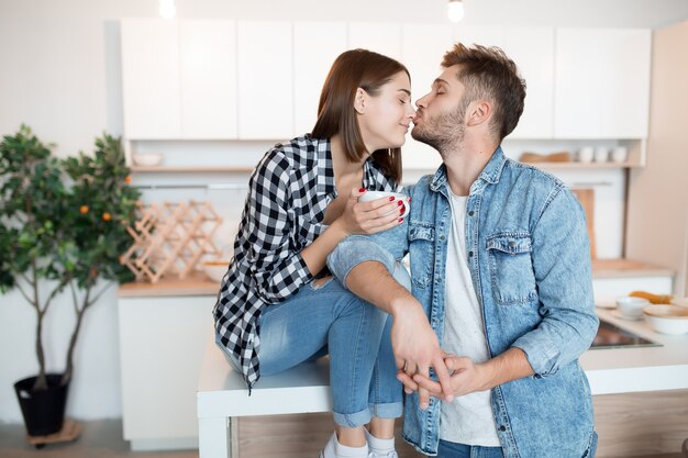 Kissing young happy man and woman in kitchen, breakfast, couple together in morning, smiling, having tea