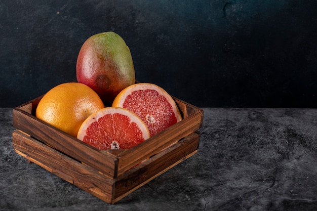 Kiwi, orange and grapefruit slices in a wooden tray on a dark marble