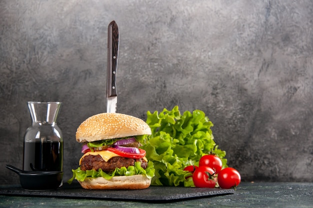 Knife in delicious meat sandwich and green pepper on black tray sauce tomatoes with stem on the right side on gray surface