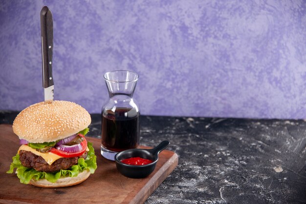 Knife in tasty meat sandwich sauce ketchup on wooden cutting board on the right side on isolated ice surface