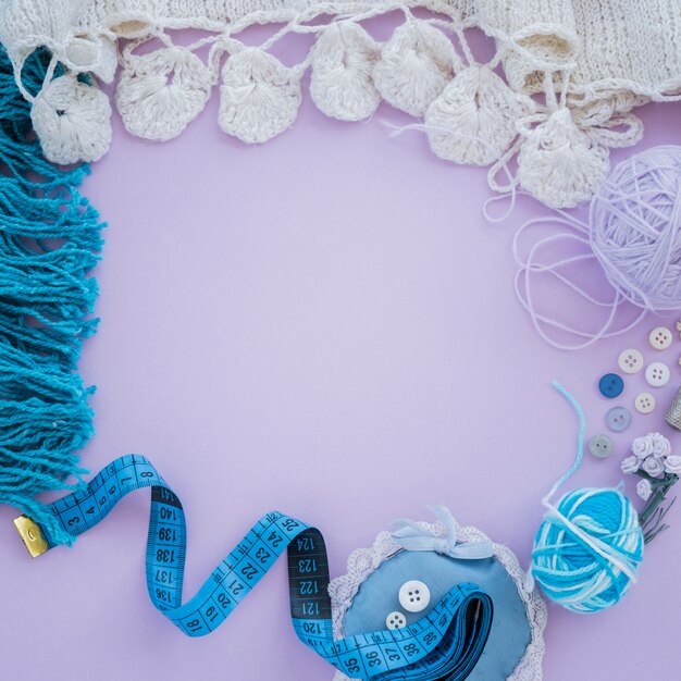 Knitted white scarf with wool; button; measuring tape on purple background