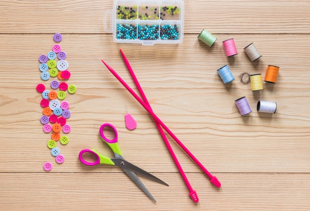 Free photo knitting needles; button; spool; beads and scissor on wooden plank