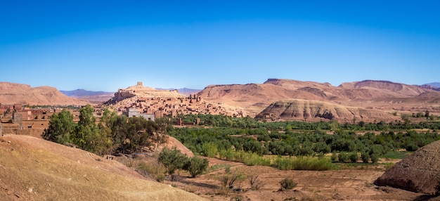 Ksar of Ait-Ben-Haddou surrounded by greenery under the sunlight and a blue sky in Morocco