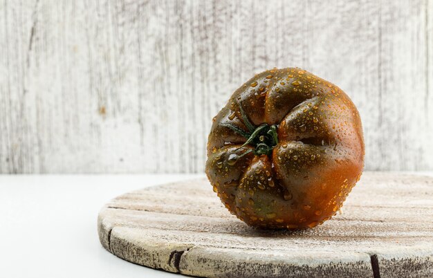 Kumato tomato on a wooden piece flat lay on white and grungy wall