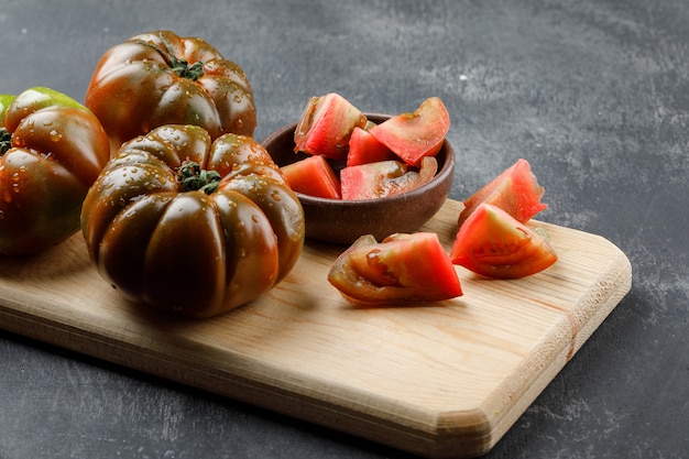 Kumato tomatoes with slices in plate on grunge and cutting board wall, high angle view.