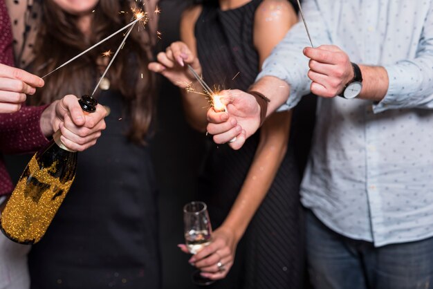 Ladies and guy holding burning Bengal lights, bottle and glass of drink 