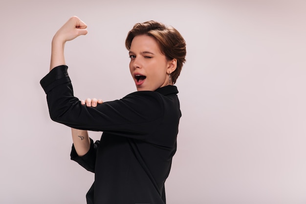 Free photo lady in black jacket shows biceps on isolated background. pretty woman in dark suit demonstrates power and muscles