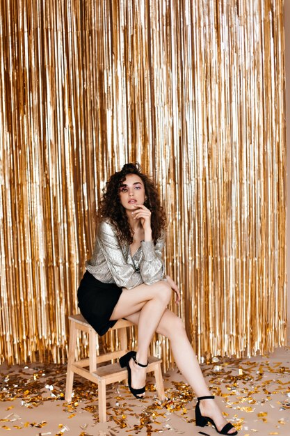 Lady in black skirt and silver top sitting on golden background