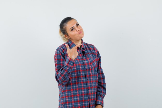 Lady in casual shirt pointing at upper right corner and looking confident , front view.