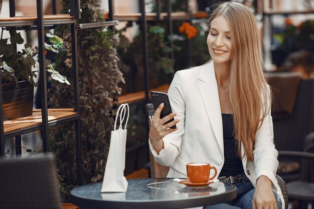 Lady drinks a coffee. Woman sitting at the table. Girl use a phone.