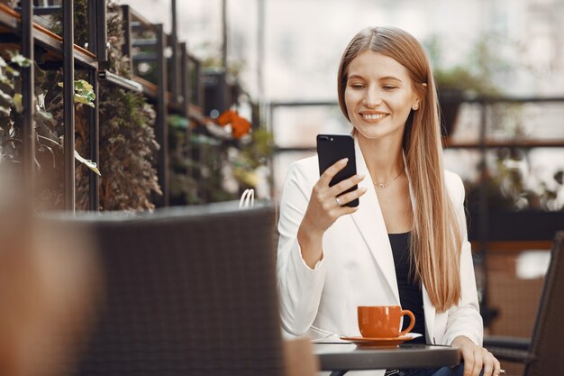 Lady drinks a coffee. Woman sitting at the table. Girl use a phone.