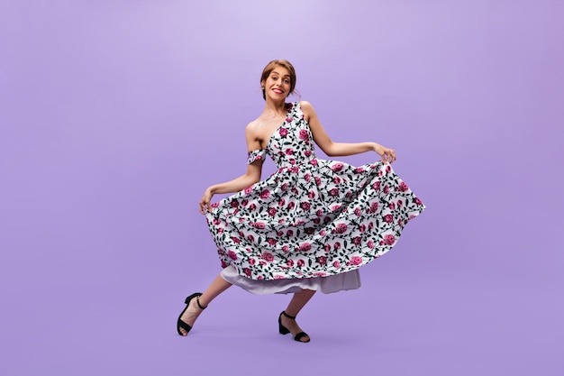 Lady in floral print dress makes reverence. Smiling fashionable woman in modern bright summer clothes posing on isolated background.