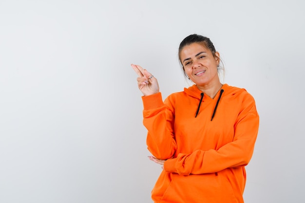 Lady gesturing with hand and two fingers in orange hoodie and looking satisfied