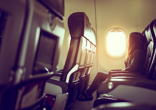 Lady is sitting in airplane looking out at shiny sun through window