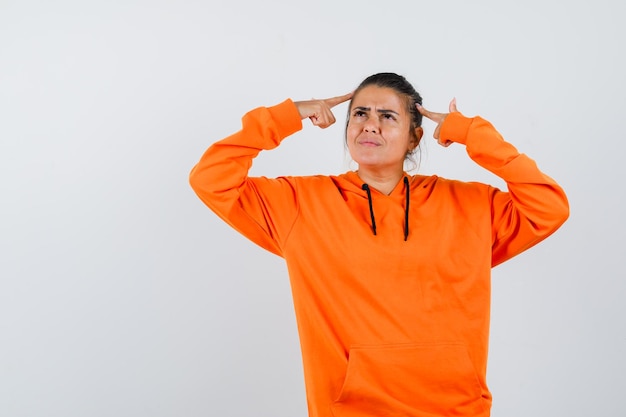 Lady keeping fingers on head in orange hoodie and looking pensive