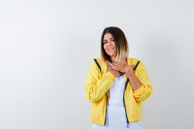 Lady keeping hands on chest in t-shirt, jacket and looking merry , front view.