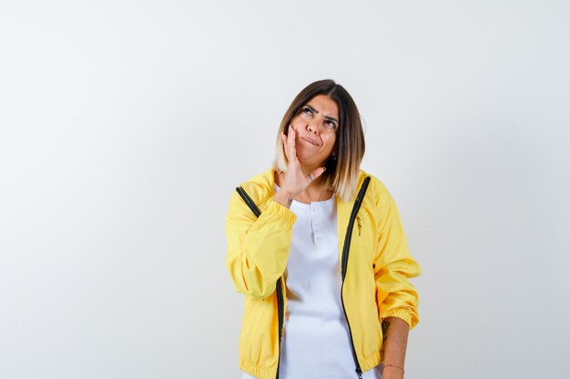 Lady leaning cheek on hand in t-shirt, jacket and looking pensive , front view.